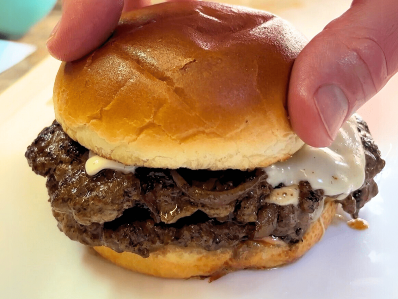 יד אוחזת בלחמניה עם המבורגר סמאש בורגר