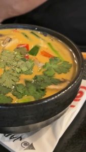 מרק מיסו בקערית שחורה עם כוסברה טרייה מעל, על גבי מפית של ג'פניקה על שולחן כהה.