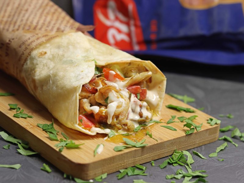 טורטייה שוכבת על קרש עץ יש בתוכה שווארמה פרגית ירקות ועלי פטרוזליה