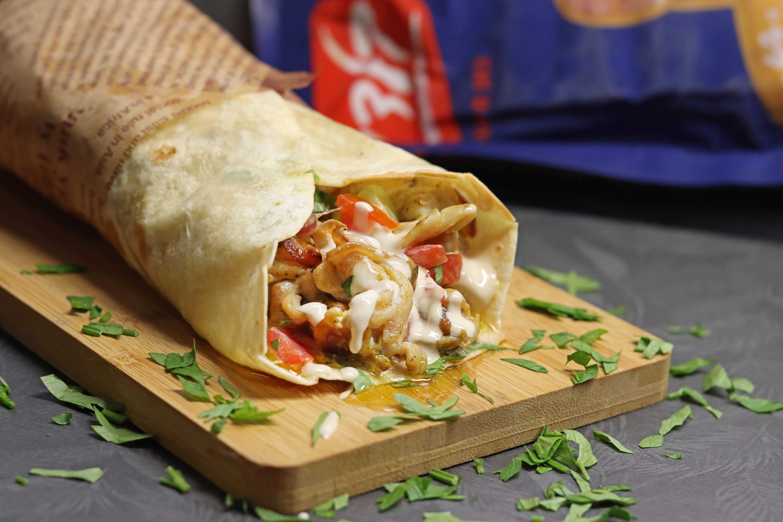 טורטייה שוכבת על קרש עץ יש בתוכה שווארמה פרגית ירקות ועלי פטרוזליה