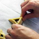 ידיים מקפלות עיגול בצק לאוזן המן עם מילוי נטולה