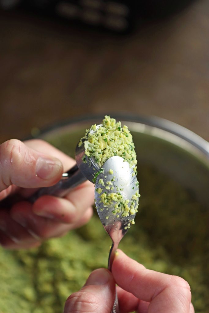 יד אוחזת במכשיר להכנת פלאפל עם תערובת חיה והיד השניה מישרת את התערובת עם כפית